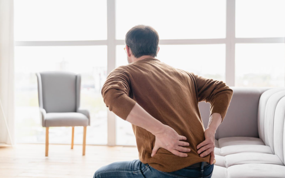 Man with recurring lower back pain getting off a couch, natural back pain treatment in Maple Ridge.