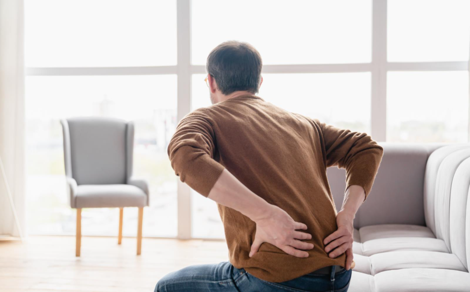 Man with recurring lower back pain getting off a couch, natural back pain treatment in Maple Ridge.