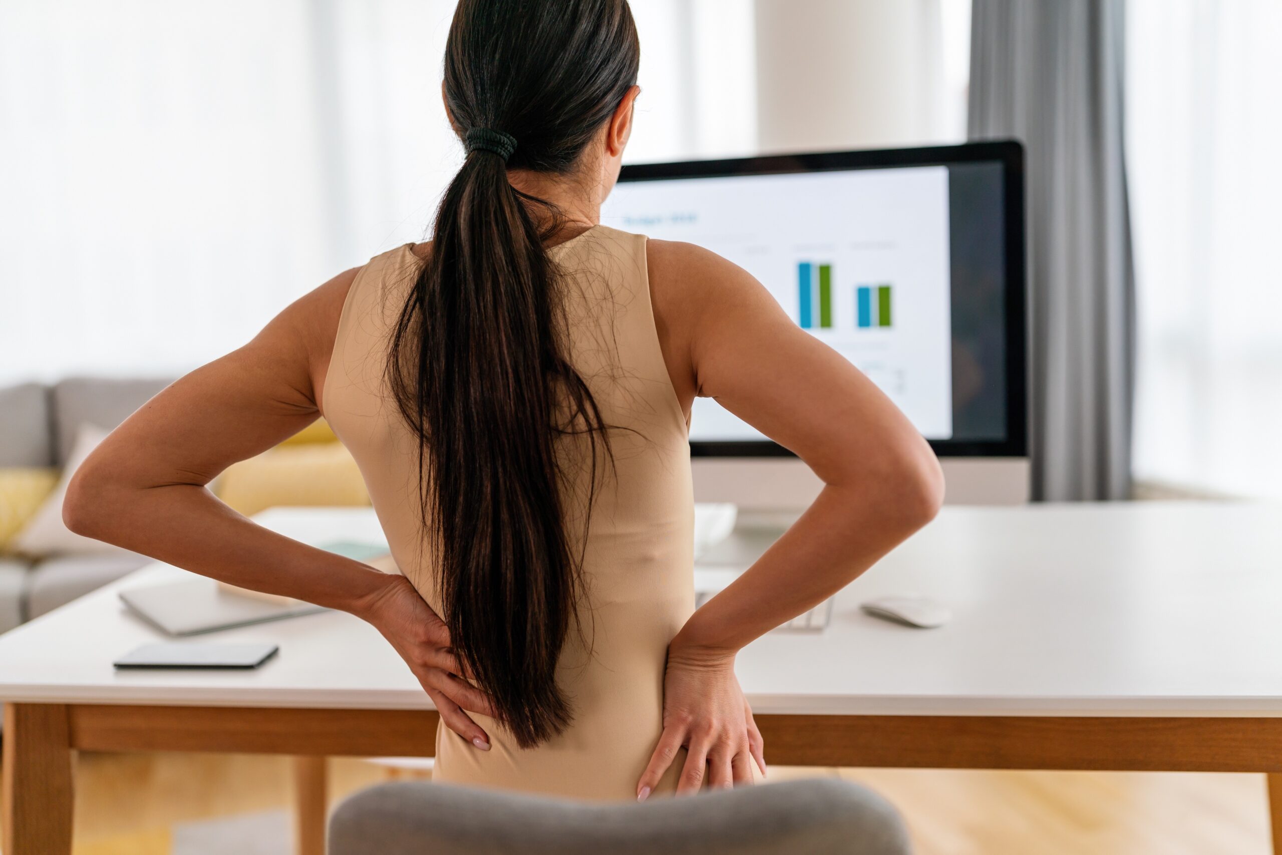 Woman working at desk with lower back pain. Posture correction and back pain treatment in Maple Ridge.