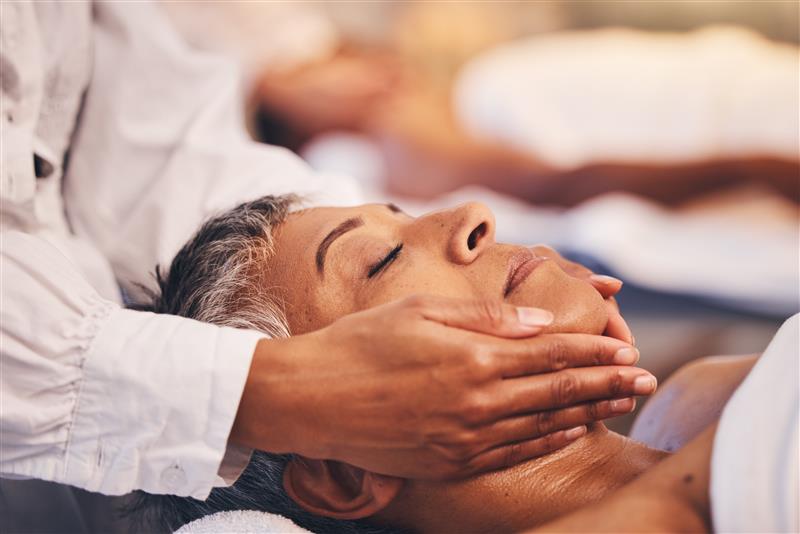 A woman with short grey-striped hair gets a TMJ-focused massage for her jaw.